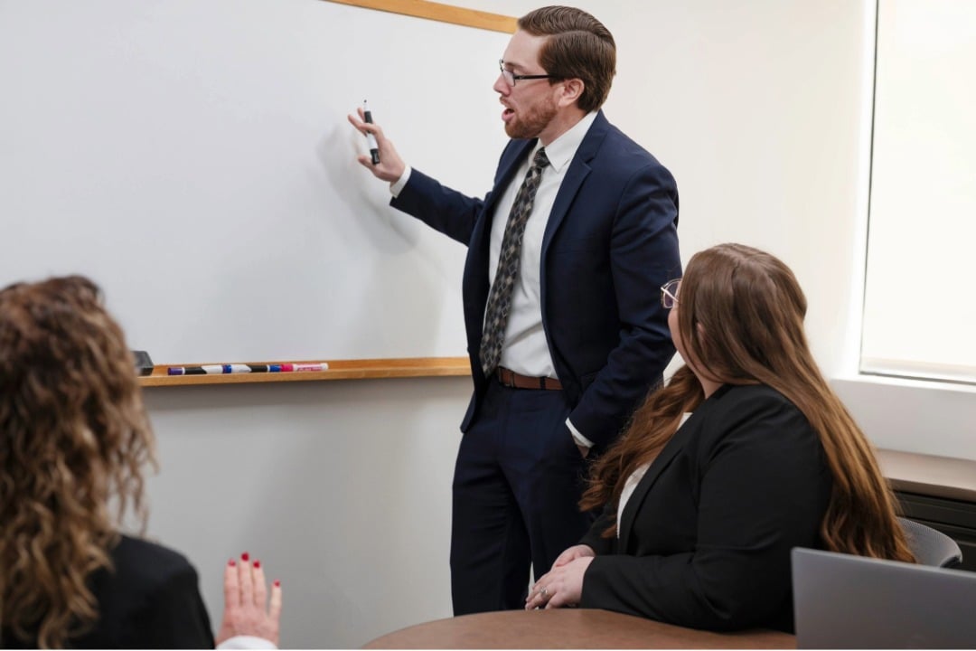 Andrew Goo, in a suit and tie, stands in front of a whiteboard, showcasing focused results for TruePlan Advisors.